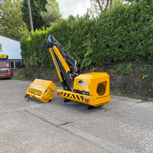 Yellow construction digger attachment parked in a lot in front of a Russell's store, with a hedge and white building in the background.