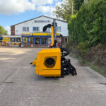 Bright yellow agricultural machine with black hoses in the foreground outside a farm equipment shop named Russell's.