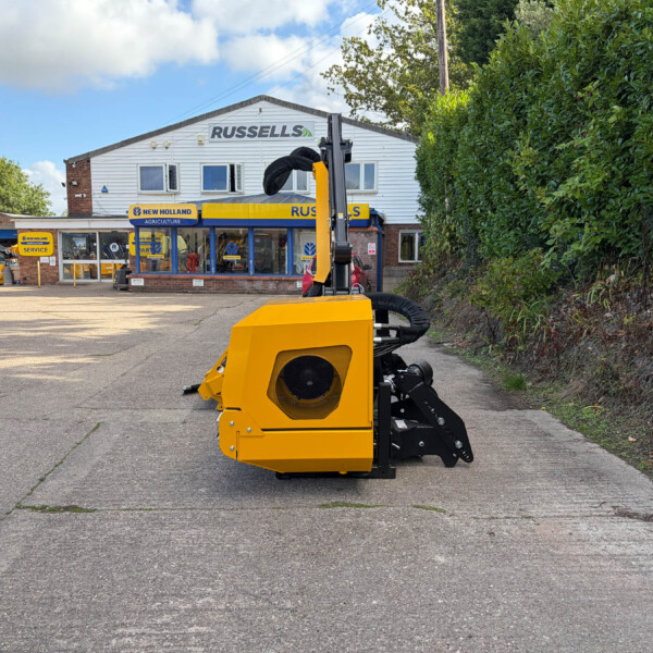 Bright yellow agricultural machine with black hoses in the foreground outside a farm equipment shop named Russell's.