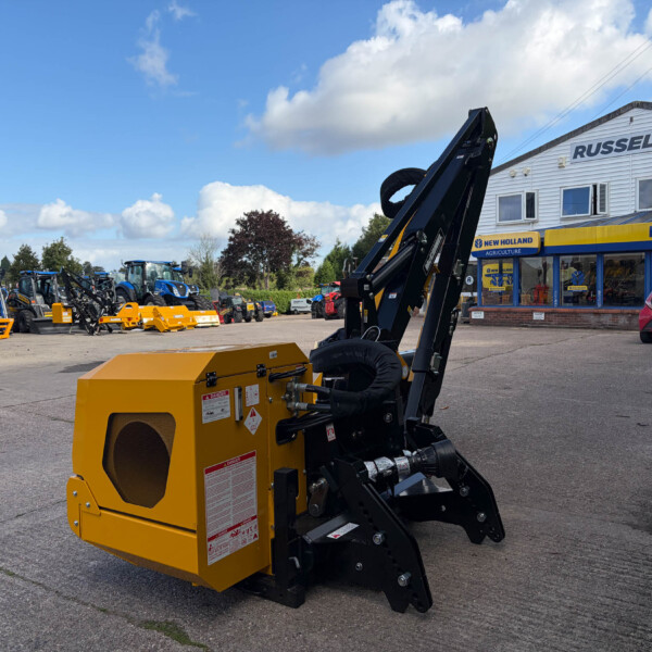 Large yellow construction attachment in the foreground at an outdoor machinery lot with blue tractors and a Russell's dealership building in the background.