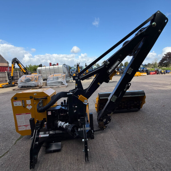 Large black hydraulic crane arm in foreground at a construction yard, with pallets, a yellow generator, and blue sky.