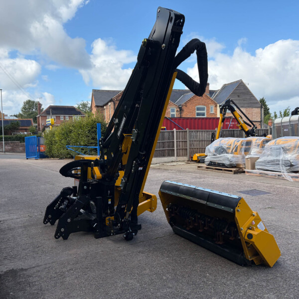 Construction machinery with a long black arm in a yard; pallets wrapped in plastic and brick houses in the background