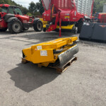 Red tractor and large red hydraulic implement in an outdoor equipment yard with yellow attachments in the foreground.