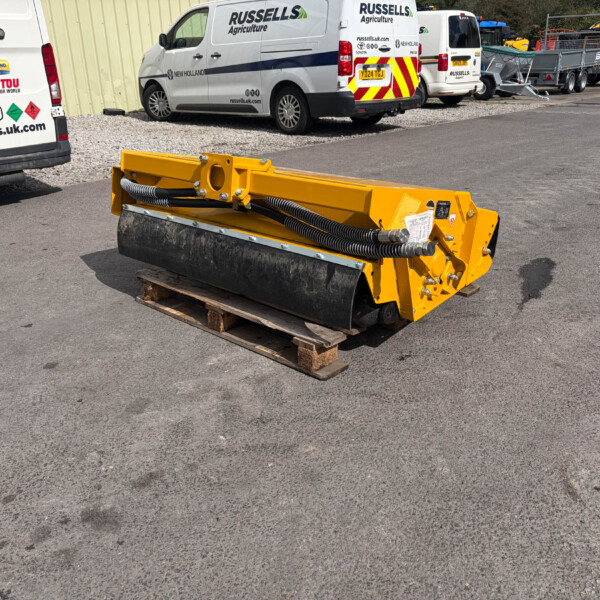Yellow road roller attachment resting on a wooden pallet in an industrial yard, with branded white vans and trailers in the background.