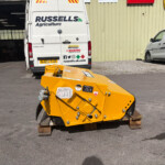 Rear view of Russell's Agriculture white van in a storage yard with another branded van nearby and a yellow industrial machine in the foreground.