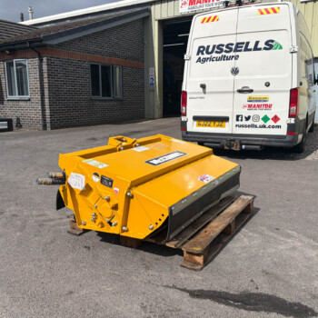 Rear view of a white van with Russell Agriculture logo parked outside a workshop, with yellow machinery in the foreground on pallets.