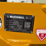 Close-up of a yellow industrial machine with a black McConnel identification plate showing model and serial details, plus a red 8 Hours safety sticker and a QR code nearby.
