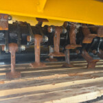 Close-up of rusted metal brackets, bolts, and gears under a yellow industrial machine frame.