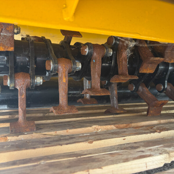 Close-up of rusted metal brackets, bolts, and gears under a yellow industrial machine frame.