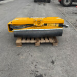 Yellow road roller sitting on a wooden pallet on an asphalt surface at a construction site, with hoses visible on the machine.