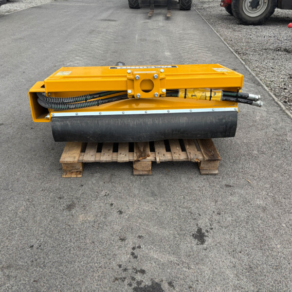 Yellow road roller sitting on a wooden pallet on an asphalt surface at a construction site, with hoses visible on the machine.