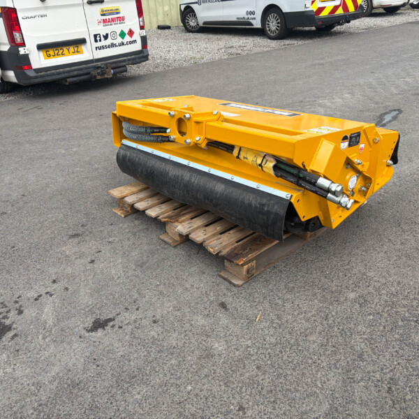 Yellow road roller/compactor resting on wooden pallets in a parking lot with white vans in the background.