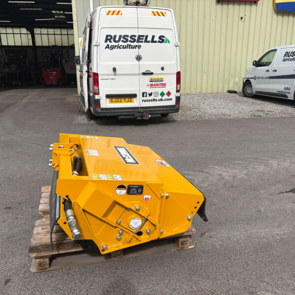 Yellow industrial machine on wooden pallets in a parking lot with white vans labeled Russell's Agriculture in the background.
