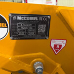 Close-up of a yellow machine showing a black identification plate with model and serial numbers, and a circular 'McConnel Inspected' sticker.