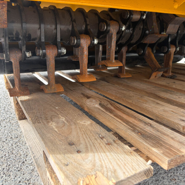 Rusty undercarriage of agricultural equipment with rusted blades and bolts, resting on a wooden pallet beneath a yellow frame.