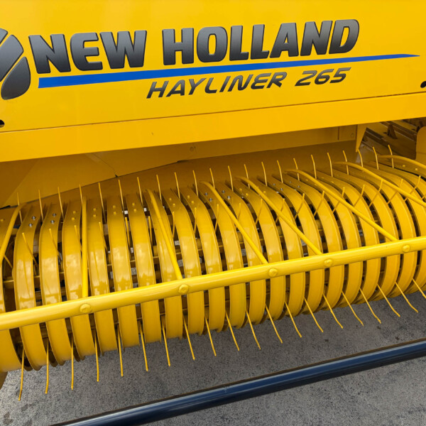 Close-up of a bright yellow New Holland Hayliner 265 harvester header, showing curved metal tines and the pickup area at the bottom.