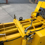 Close-up of a bright yellow industrial machine showing hydraulic components, metal beams, and hoses.