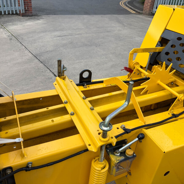 Close-up of a bright yellow industrial machine showing hydraulic components, metal beams, and hoses.