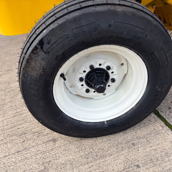 Close-up of a heavy-duty black tire with a white rim, mounted on yellow industrial equipment behind it on concrete.]","Wheel and tire: black treaded tire with white rim, part of yellow machinery visible in the background.