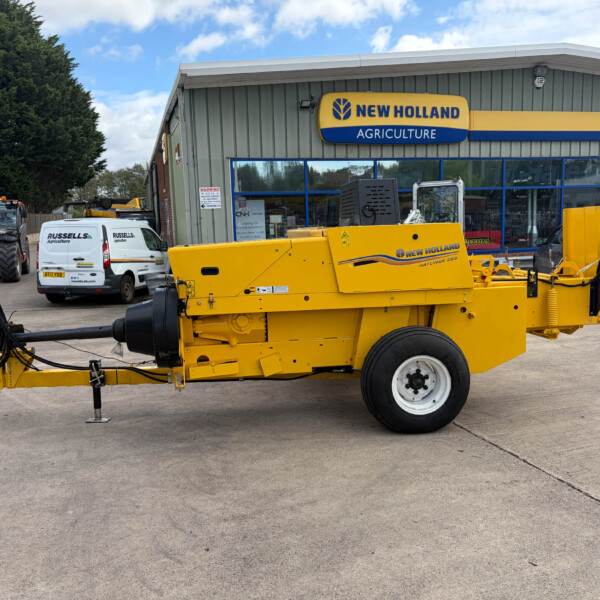 Yellow New Holland Hayliner baler in front of Russell's Agriculture shop, blue and yellow storefront sign above the building.