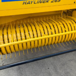 Close-up of a yellow combine harvester header reel with curved tines for gathering crops.