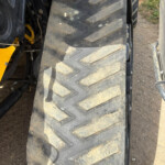 Close-up of a large tractor tire with deep tread, dusty and muddy, showing part of the yellow tractor frame.