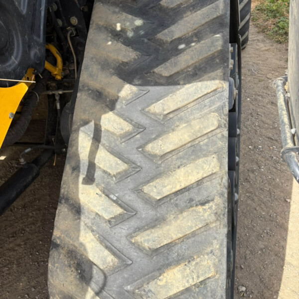 Close-up of a large tractor tire with deep tread, dusty and muddy, showing part of the yellow tractor frame.