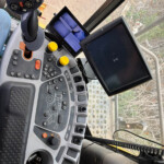 Close-up of a tractor cabin control panel with a joystick, yellow knobs, and two screens visible inside the cab