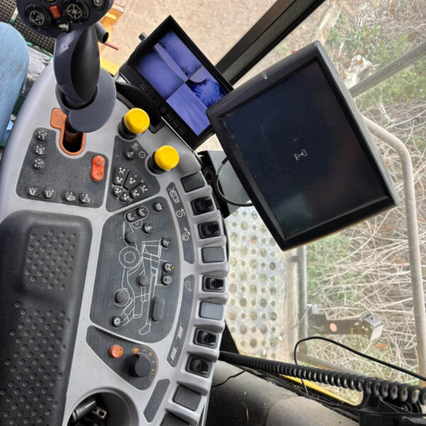 Close-up of a tractor cabin control panel with a joystick, yellow knobs, and two screens visible inside the cab