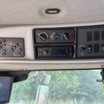 Interior of a truck cab showing climate control dials and dashboard panels with a monitor on the left and a yellow warning sticker on the right panel