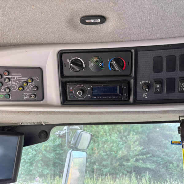 Interior of a truck cab showing climate control dials and dashboard panels with a monitor on the left and a yellow warning sticker on the right panel