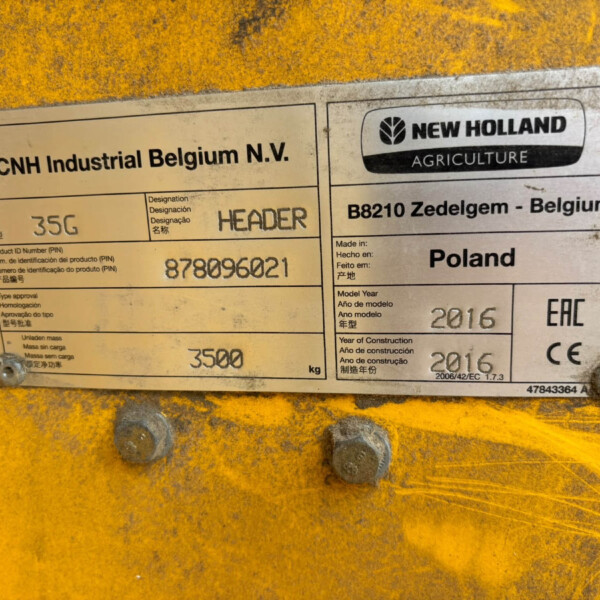 Metal nameplate on yellow equipment showing company name CNH Industrial Belgium N.V. and New Holland Agriculture.