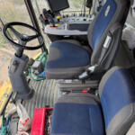 Interior of a tractor cab with steering wheel, control panel, and mounted display screen facing the driver
