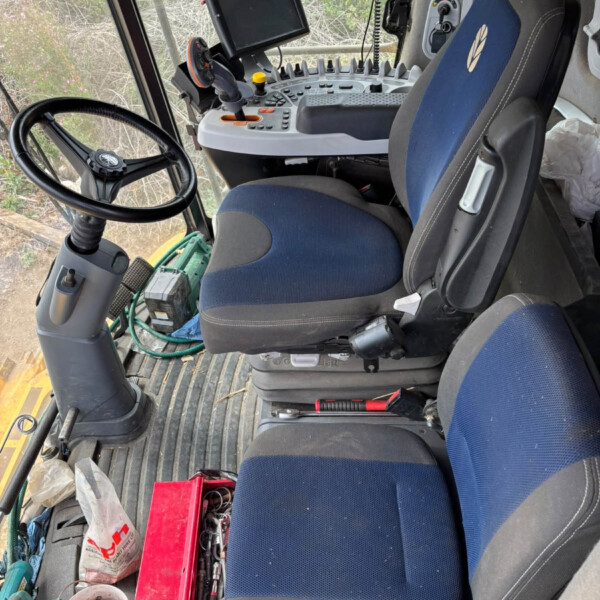 Interior of a tractor cab with steering wheel, control panel, and mounted display screen facing the driver