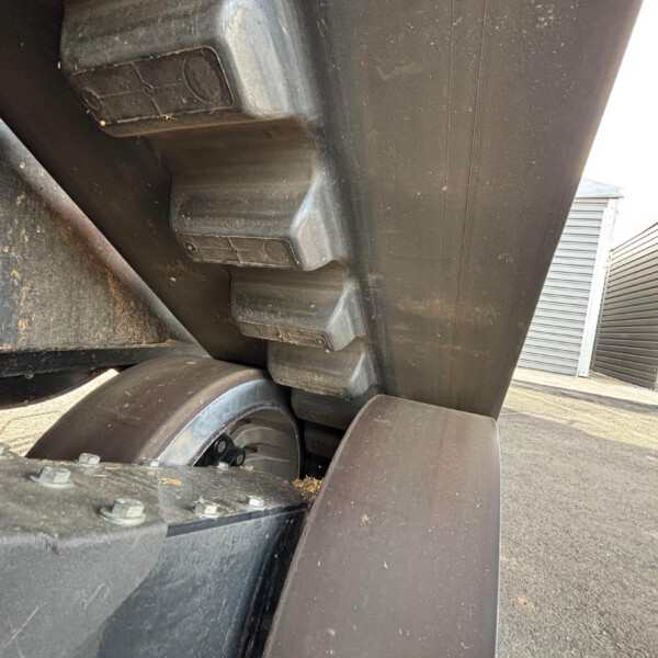 Close-up of the underside of a large black trailer with a wheel and metal supports, dirt and grime visible on the surface.