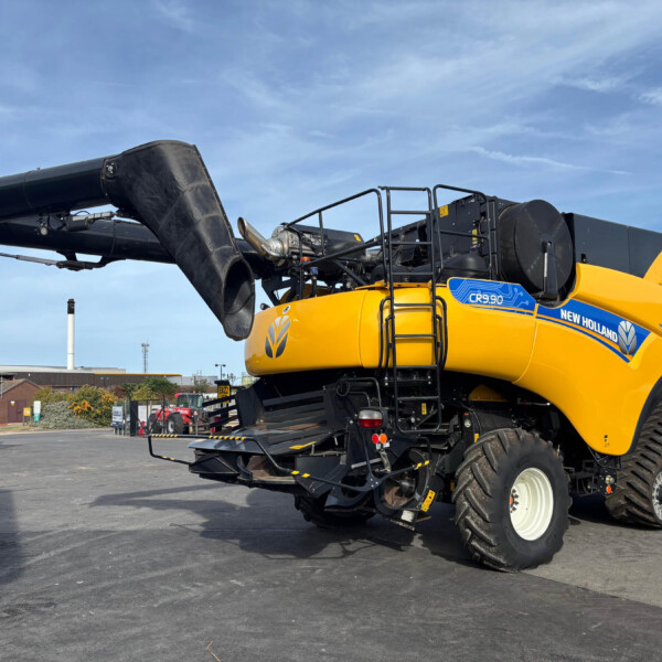 Side view of a yellow New Holland CR9.90 combine harvester with a large black auger extending to the left under a clear blue sky.
