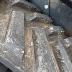 Close-up of worn black rubber tires or belts with deep grooves and scuffed surfaces, piled together in a dark industrial setting.
