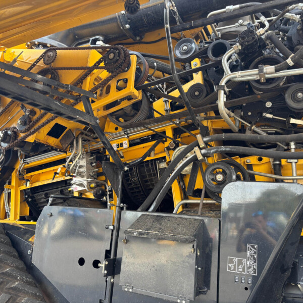 Close-up of yellow heavy machinery's belt drive, pulleys, and hydraulic hoses.