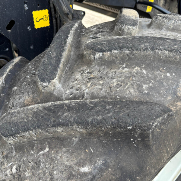 Close-up of a muddy tractor tire tread with a black metal hitch/frame and a small yellow warning sticker in the background