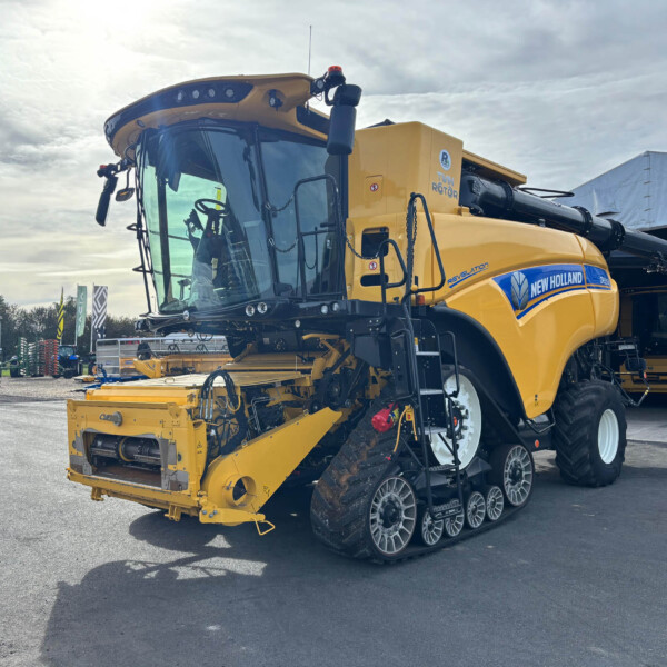 Agricultural combine harvester in yellow, parked beside a building with oversized tires and crop headers attached at the front.