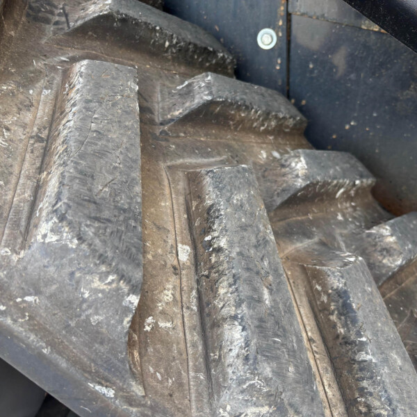 Close-up of worn black rubber tires or belts with deep grooves and scuffed surfaces, piled together in a dark industrial setting.