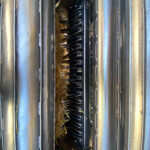Internal view of a grain auger mechanism between metal rollers, with straw around the blades