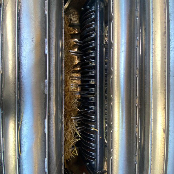 Internal view of a grain auger mechanism between metal rollers, with straw around the blades