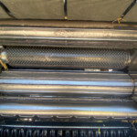 Close-up of a dirty metal harvester header with rotating cutting blades and straw underneath.