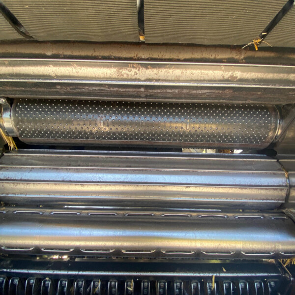 Close-up of a dirty metal harvester header with rotating cutting blades and straw underneath.