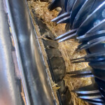 Interior of a metal machine with sharp blades and packed straw or chaff between parts, suggesting a grain or hay processing area.