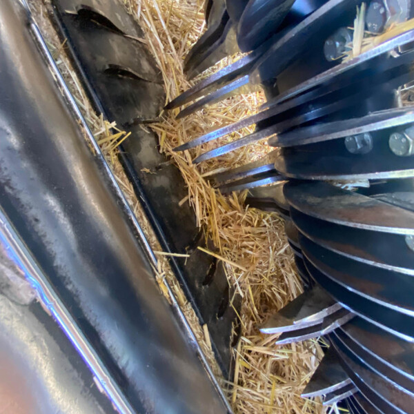 Close-up of a farming machine interior with metal blades and straw scattered around, likely part of a baler or combine.