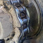 Close-up of a dirty metal bearing on a machinery hub, with mud and debris caked around the slotted rollers.