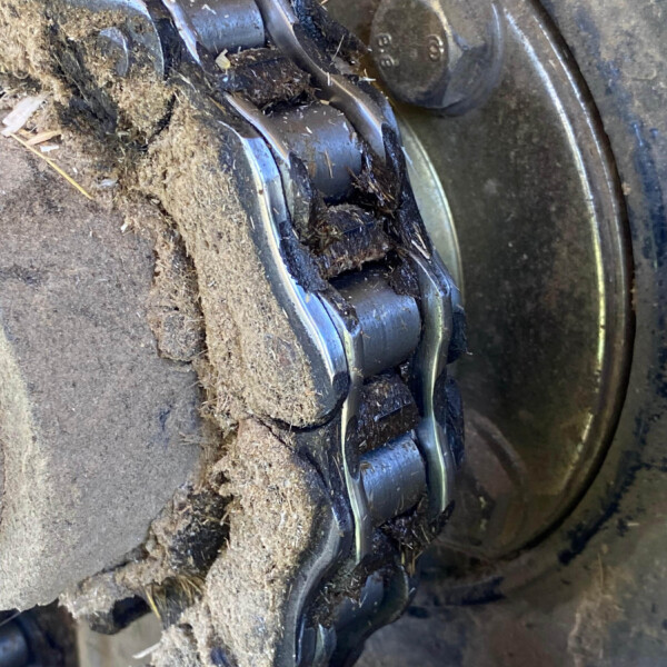 Close-up of a dirty metal bearing on a machinery hub, with mud and debris caked around the slotted rollers.