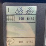 Car dashboard display panel showing a cluster of circular icons and the letters 'L', with an odometer-like readout showing numbers 106 6150.